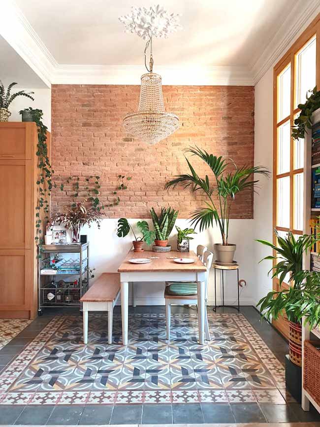 This small living room with dining table blends a bold brick wall, an ornate chandelier, and colorful tiled floors for a cozy rustic-chic vibe.