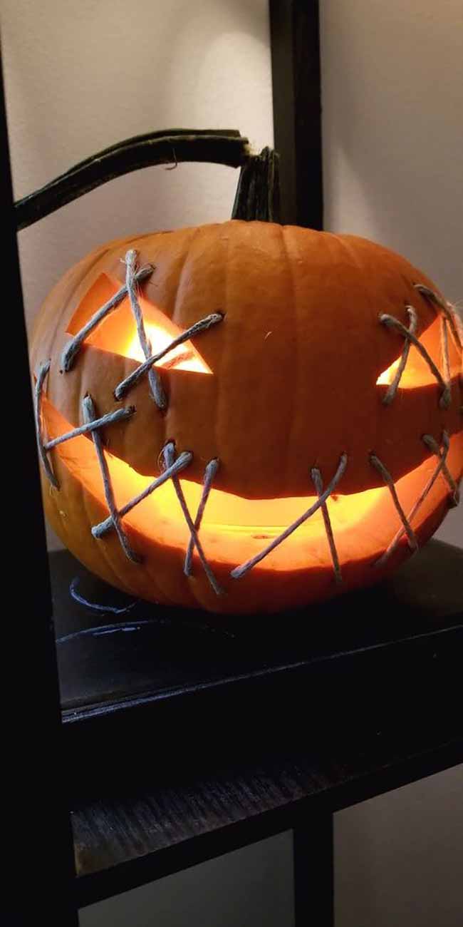 This pumpkin looks like it's trying to keep a secret, with its eyes and mouth sewn shut with thick string.