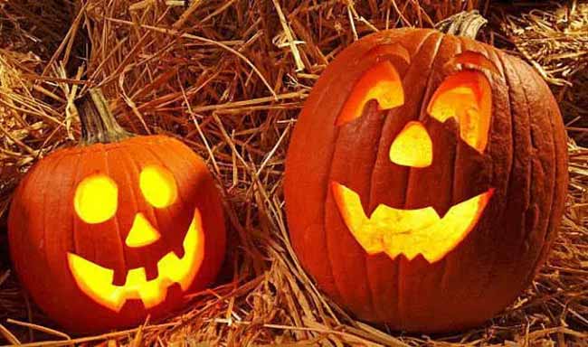 Two jack-o'-lanterns are glowing warmly in a pile of hay, a perfect autumn scene. This is such a cozy pumpkin carving display.