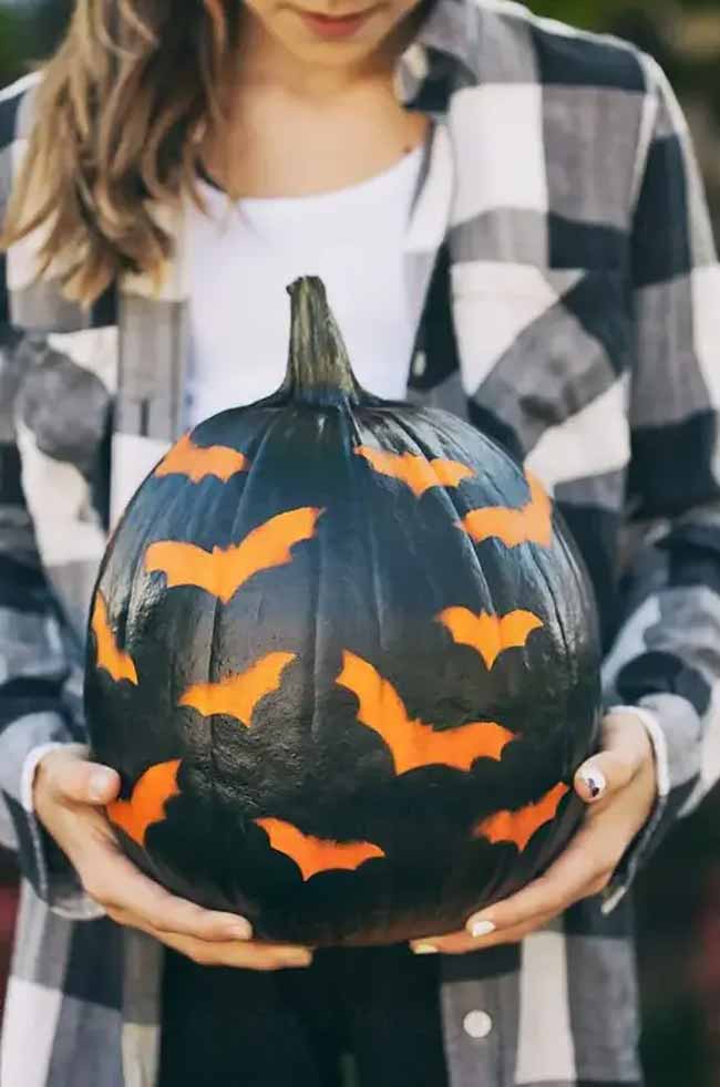 Painted in matte black, the pumpkin highlights the bright orange bats scattered across its surface.