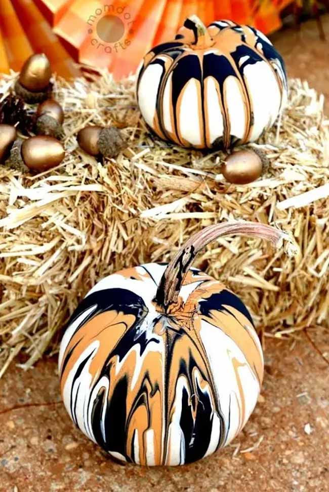 Two pumpkins sitting on a hay bale have a cool marbled effect, created by pouring black, orange, and white paint over the top and letting it drip down the sides.