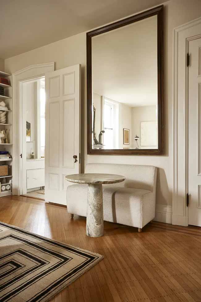 A tall wood-framed mirror reflects a plush bench and marble table, making the dining nook feel bigger than it is.