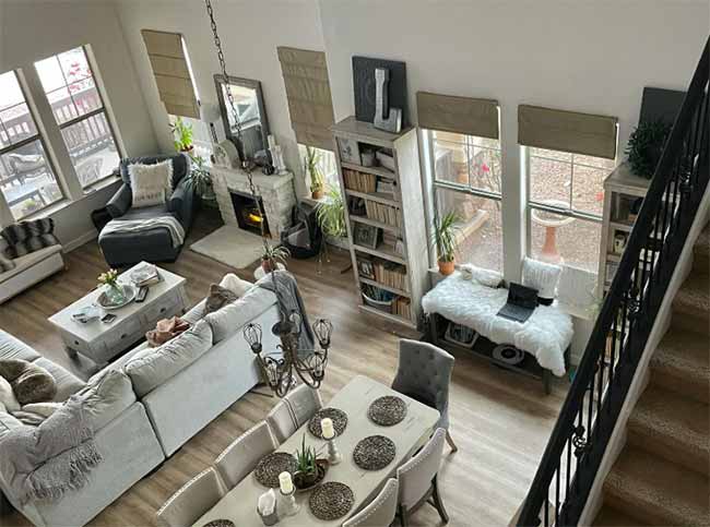 From above, a gray sectional and long dining table with upholstered chairs are bathed in natural light in this open-plan room.