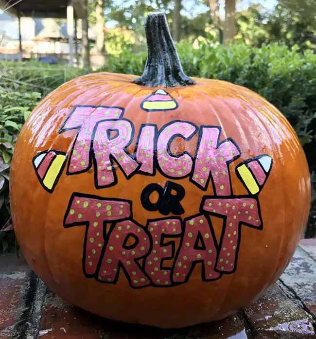 A classic orange pumpkin is hand-painted with the phrase "Trick or Treat" in fun, bubbly pink letters, with a few little candy corns for extra decoration.