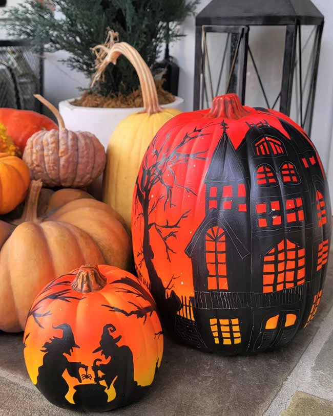 A large pumpkin shows a black haunted house against a fiery sky next to a smaller one depicting two witches over a cauldron.