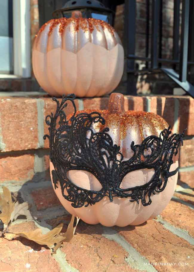 A pale pink pumpkin is given a touch of  glamour with a black lace mask tied around it and a dusting of orange glitter on top.