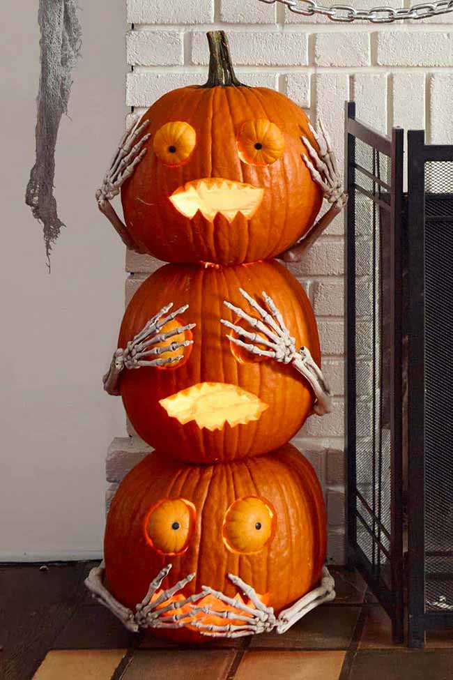 This pumpkin carving stacks three pumpkins on top of each other, with each one doing a different pose inspired by the "see no evil, hear no evil, speak no evil" monkeys. Skeleton hands are attached to the pumpkins to cover their eyes, ears, and mouth.