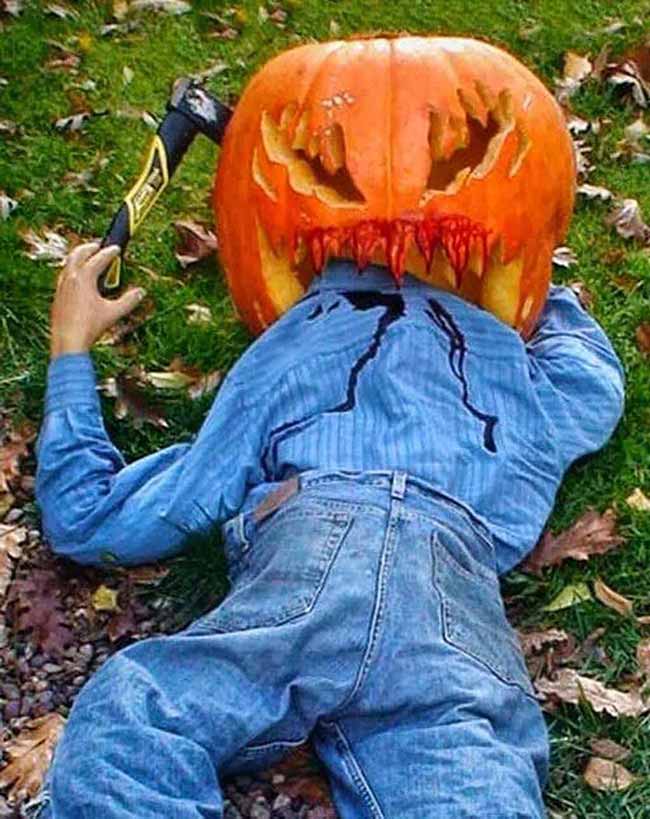 This spooky pumpkin carving is part of a Halloween decoration that looks like a headless person holding an axe. The carving is placed on top of the figure's neck, with red "blood" dripping down.