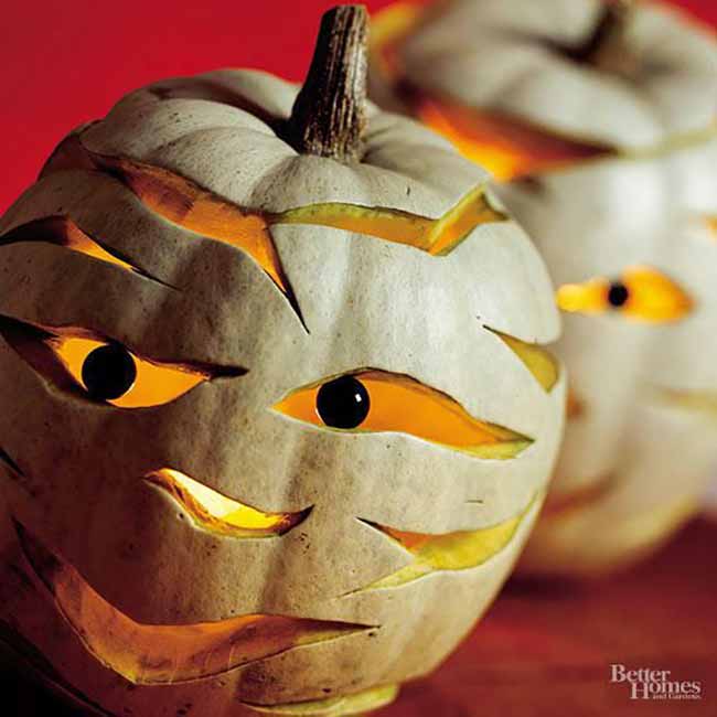 These two pumpkins are designed to look like mummies, with horizontal slits carved across their bodies and bright, glowing eyes.