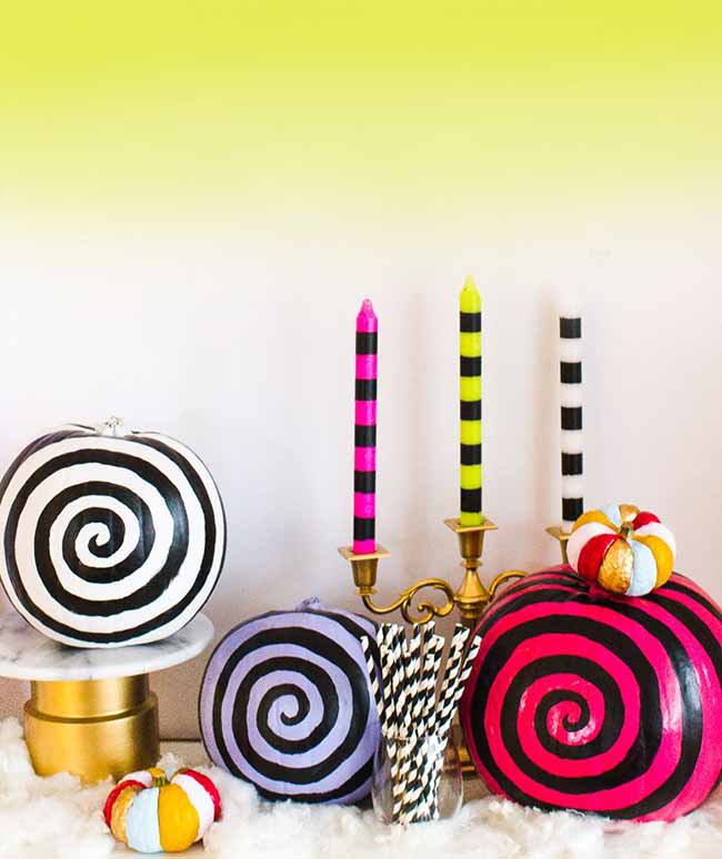 A bold Halloween display features spiral-painted pumpkins in black-and-white and pink-and-black, arranged with matching striped candles.