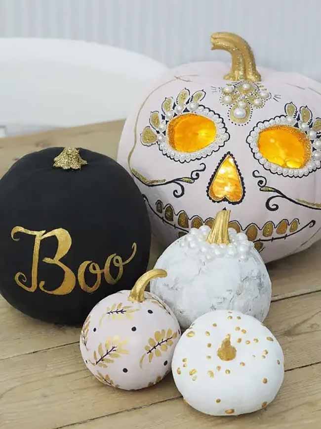 A chic pumpkin collection includes a matte black “Boo” pumpkin in gold script and a larger skull pumpkin outlined with gold paint and pearls.
