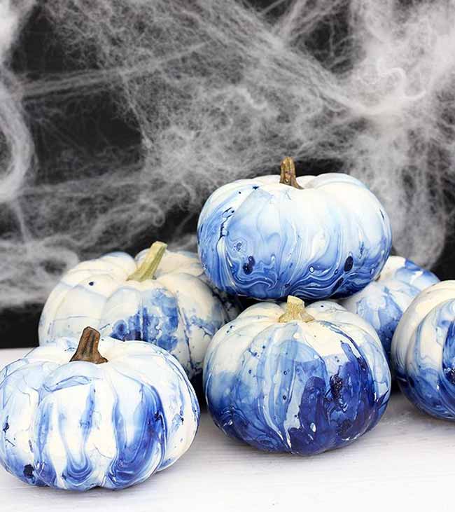 Small white pumpkins with a blue-and-white marbled effect resemble porcelain and are displayed in front of white spiderwebs.