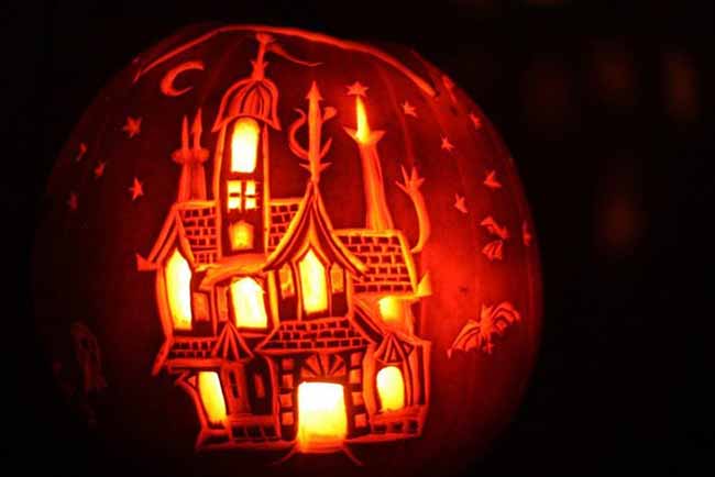 A spooky haunted house scene is intricately carved into this pumpkin. The light from inside highlights all the details, from the moon to the bats.