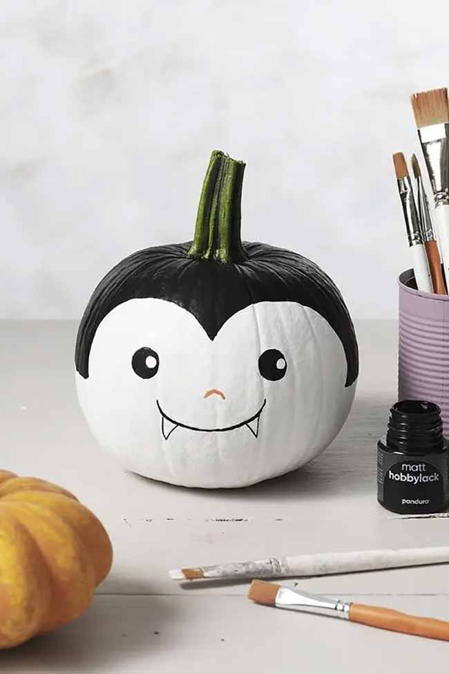 A festive white pumpkin is painted with a cartoon-style Dracula face, complete with a widow’s peak and tiny fangs for a fun, spooky look.