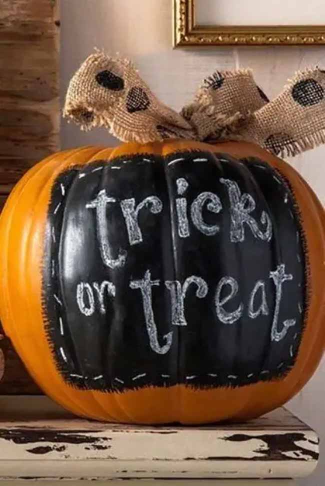 A pumpkin features a rectangular chalkboard-like panel with “trick or treat” written in casual handwriting, topped with a burlap bow.