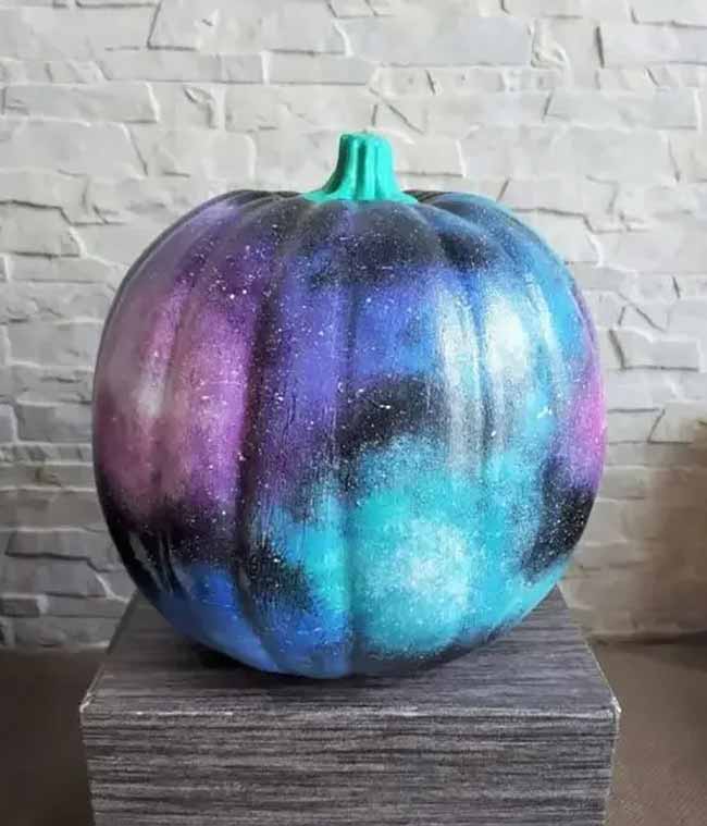 This single pumpkin has been spray-painted to look like a swirling galaxy, with deep purples, blues, and blacks blending together and speckled with white like a field of stars.