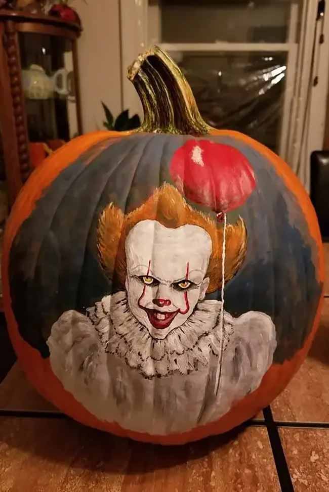 An impressive pumpkin is hand-painted with a detailed portrait of the clown Pennywise holding a red balloon, creating a truly creepy effect.