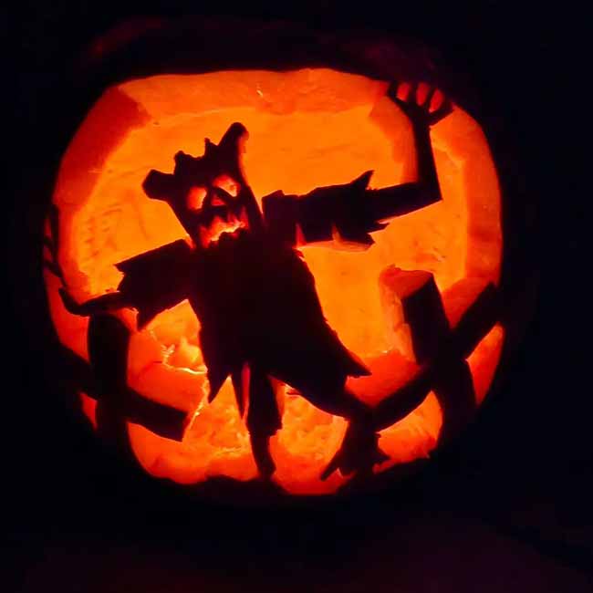 A spooky scarecrow is carved into this pumpkin, looking like it's reaching out from the darkness.