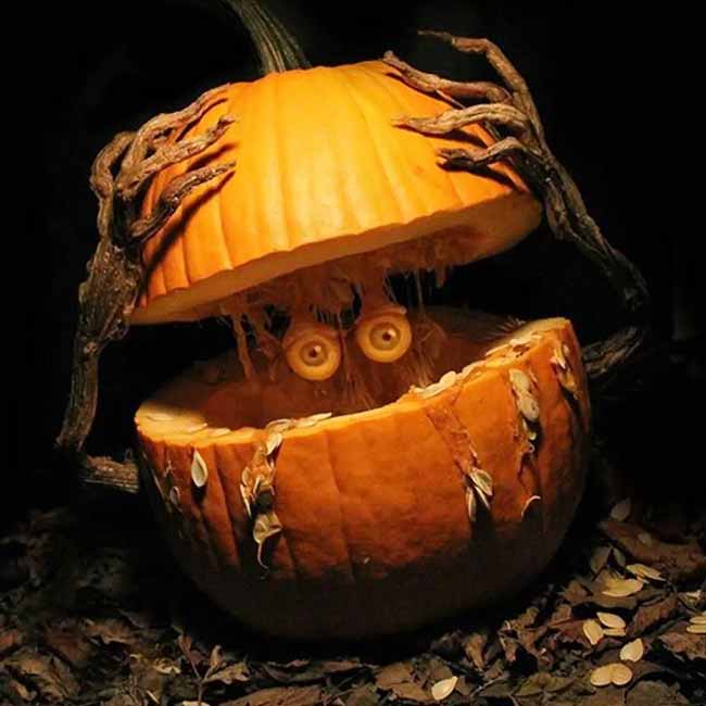 This pumpkin carving looks like a spooky creature is bursting out of the ground. It has carved, branch-like arms that hold its top half up, revealing a pair of creepy eyes inside.