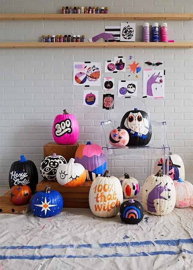 A colorful pumpkin display mixes bold designs, from a bright pink “BOO” to a detailed white spiderweb on black, for a playful Halloween arrangement.