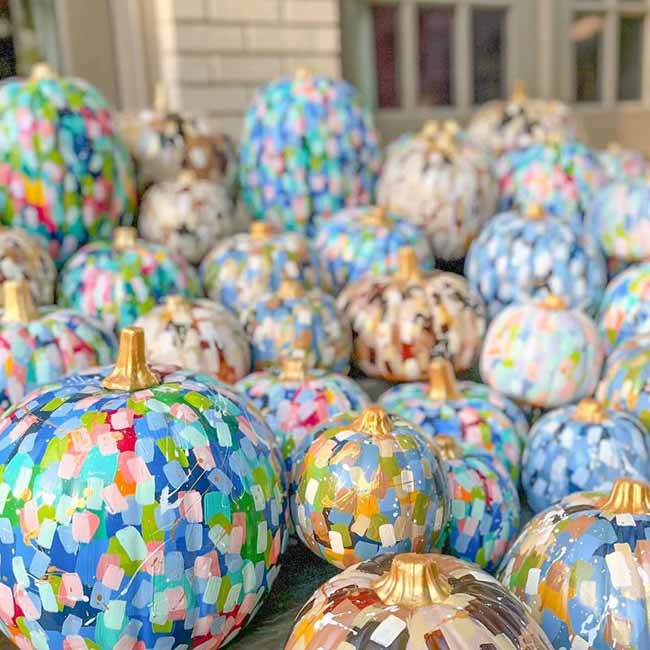 A large pile of pumpkins sits outside, each painted with a vibrant, abstract mosaic of colorful brushstrokes in a style reminiscent of impressionist art.