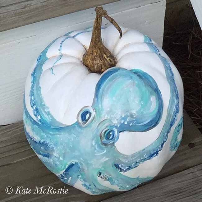 A white pumpkin is hand-painted with a swirling blue octopus, its curling tentacles wrapping elegantly around the sides.