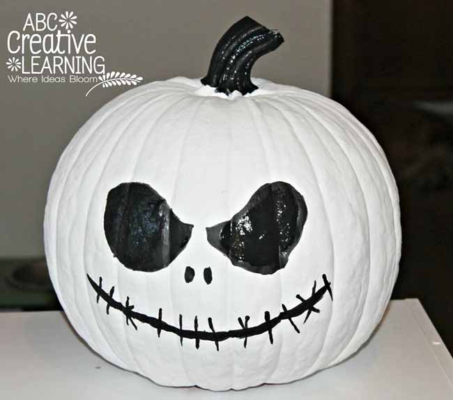 A big white pumpkin is decorated with a detailed black face, including a stitched mouth and large dark eyes, resembling Jack Skellington from The Nightmare Before Christmas.