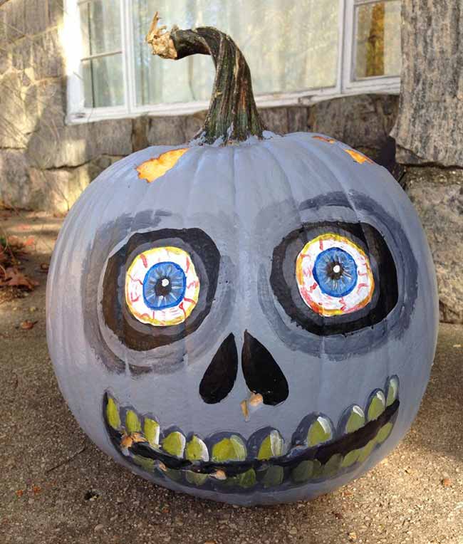 A gray pumpkin is painted with a slightly faded face, featuring bloodshot eyes with vibrant blue irises for a creepy, zombie-like look.