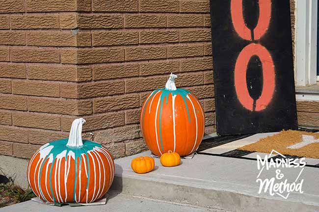 Two pumpkins sit on a front step, painted with turquoise dripping from their white stems for a playful pop of color on the porch.
