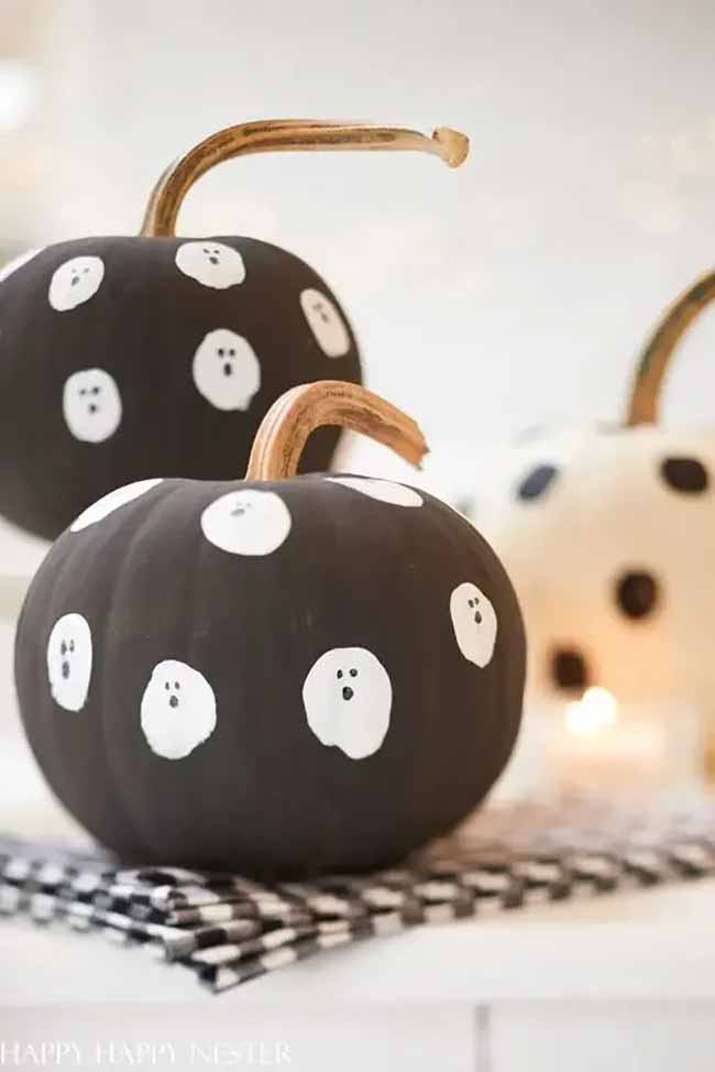 Two dark pumpkins are decorated with white polka dots, each dot revealing a tiny ghostly face for a whimsical indoor scene.