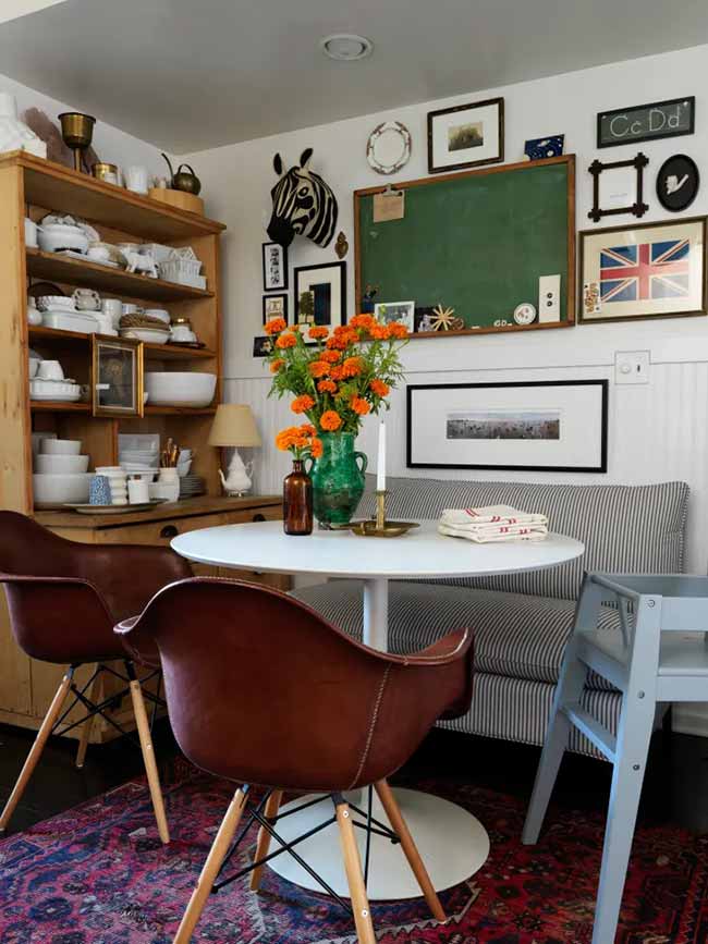 A small living room with dining table fits neatly in the corner with a striped bench, leather chairs, and a fun gallery wall.