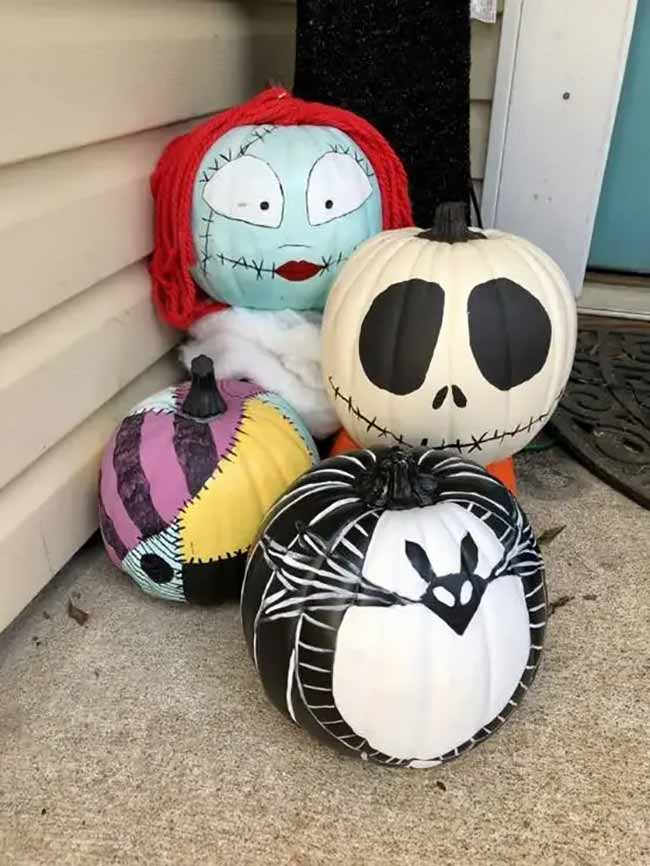 A whimsical group of pumpkins leans against a house, including one styled as Sally from The Nightmare Before Christmas with red yarn hair, and another painted like Jack Skellington’s face.