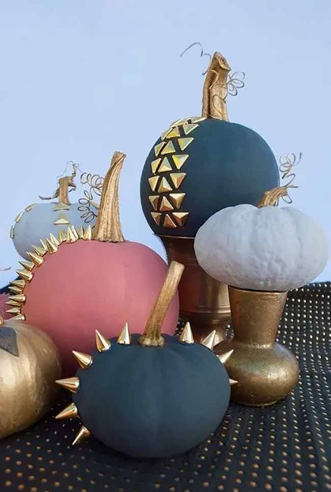 Several uniquely decorated pumpkins are grouped together, featuring textures and embellishments like metallic spikes and geometric shapes on colored bases.